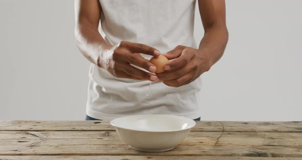 Video of biracial man cracking egg into white bowl on wooden surface and white background