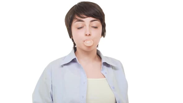 Young Smiling Caucasian Girl with Short Haircut Chewing Gum and Blowing Bubble Over White Background