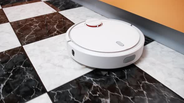 The Robot Vacuum Cleaner Cleans in the Modern House on the Tiles Floor at Kitchen