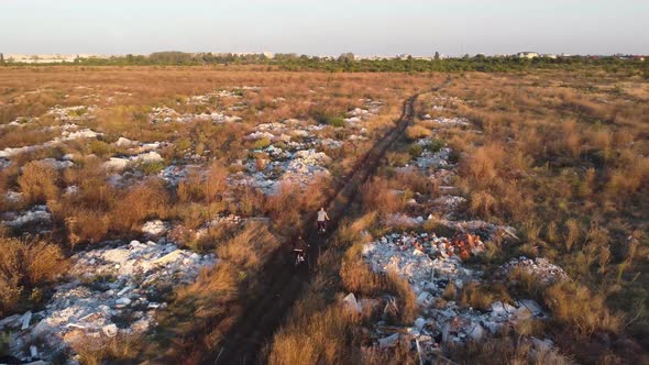 Aerial View of 2 Bikers Riding a Path Full of Waste Garbage Land Close to a City