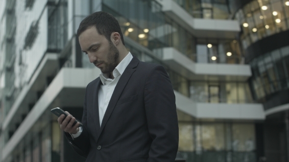 Young Businessman Reads a Text Message Standing