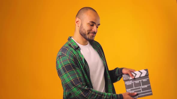 Casual Young African American Man Claps Clapperboard Against Yellow Background