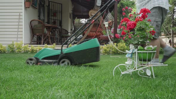 An old man mowing the grasses in his lawn with a electrical lawn mower.
