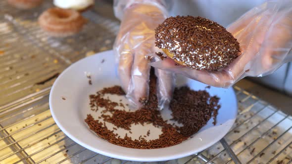 Hands in a Disposable Gloves Sprinkle Freshly Baked Doughnut with Chocolate