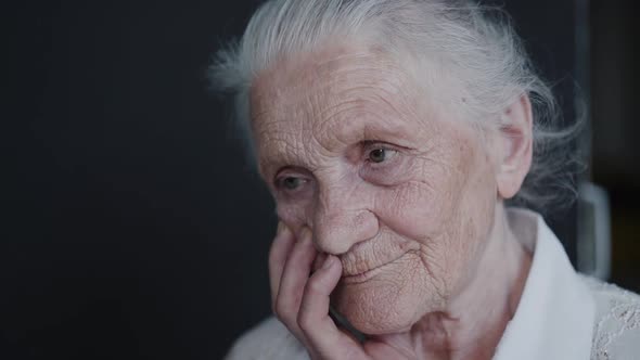 Portrait of Tired Grandmother Leans on Hand and Looks at Camera on Background