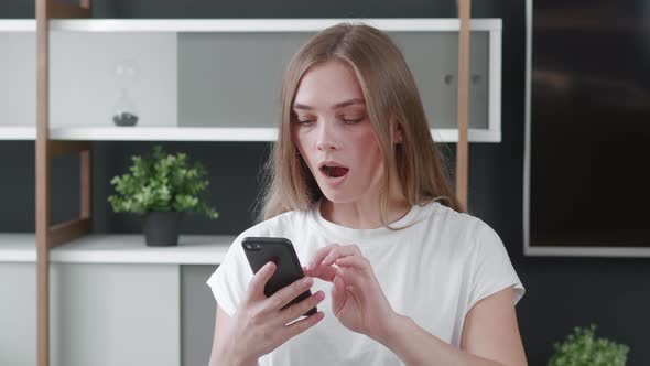 Worried Woman Reading Bad News in Message on Her Smartphone at Home Office. Shocked Young Female