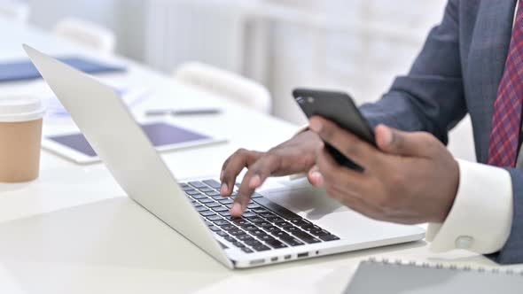 Close Up of African Man Using Smartphone and Working on Laptop