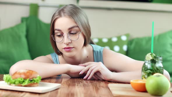 Upset Young Beautiful Woman Choosing Between Healthy Fresh Products and Harmful Fast Food