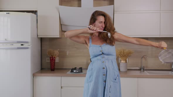 Pregnant Mom Listening Music and Dancing at Home at Kitchen. Portrait Woman Standing in Kitchen