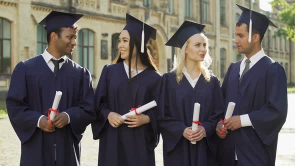 Graduate Students in Academic Regalia Talking and Looking Into Camera, Smiling