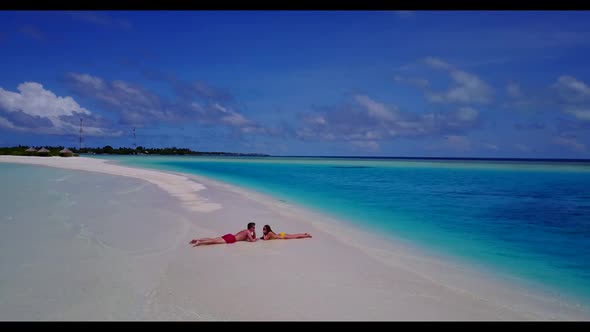 Young couple tanning on tranquil lagoon beach wildlife by turquoise lagoon and white sandy backgroun