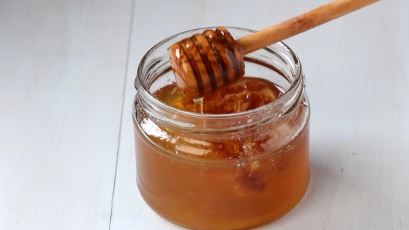 Open Glass Jar Of Liquid Honey With Honeycomb