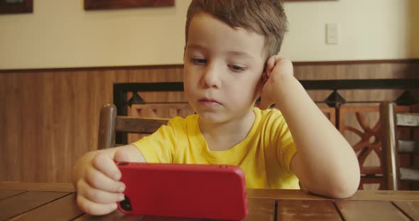 Portrait of a Child Looking at the Phone Sitting at the Table a Preschool Kid Uses Artificial