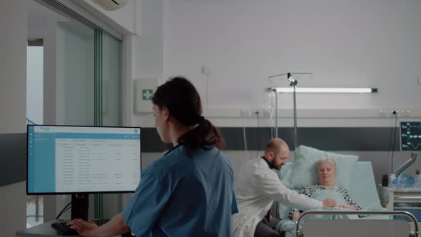 Woman Working As Nurse and Looking at Computer with Files