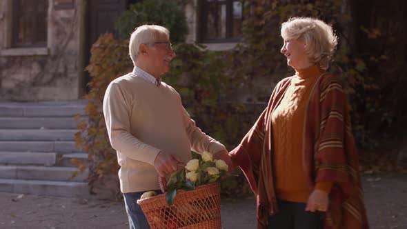 Handsome senior couple walking with basket full of flowers and groceries in autumn park