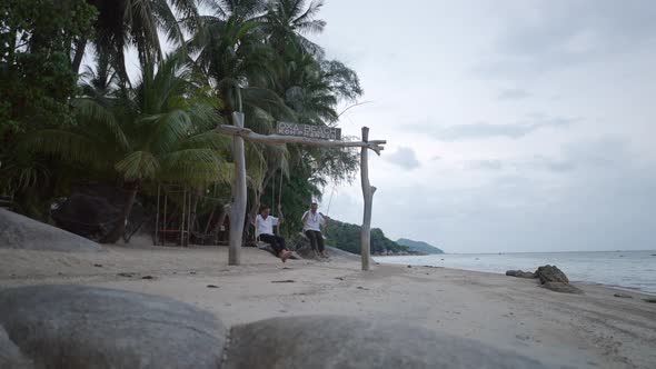 Caucasian Male Gay Couple Swinging on Swing on a Beach with Tropical Palms at Koh Phangan Island