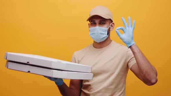 Young Pizza Delivery Man with Face Mask and Gloves Holding Pizza Boxes and Showing Ok Sign