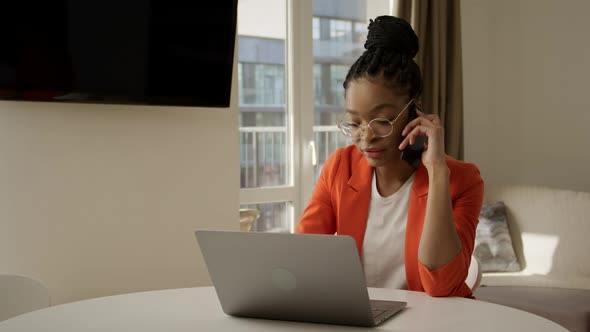 Young African American Woman is Talking on a Phone From a Home Office