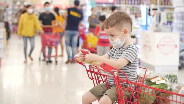 Mom with Children Makes Purchases in the Hypermarket, the Child Sits in a Protective Mask From