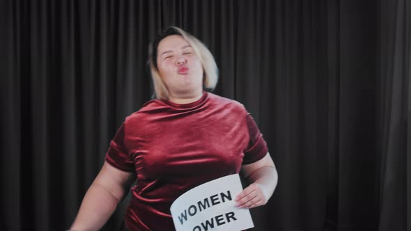 A Confident Flirty Fat Woman Holding a Nameplate with a Sign WOMEN POWER