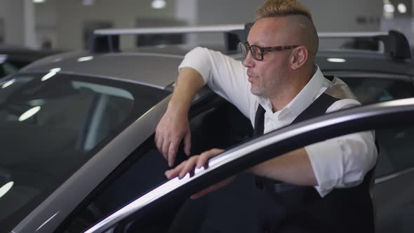 Side View of Man Admiring Brand New Car Touching Door Standing at Vehicle in Dealership