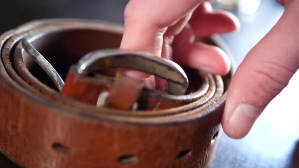 A man placing his worn out vintage leather belt and buckle on a table after a hard days work in slow