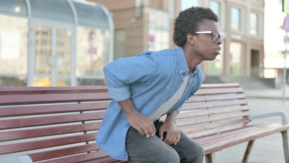 Young African Man Having Back Pain While Sitting on Bench Outdoor