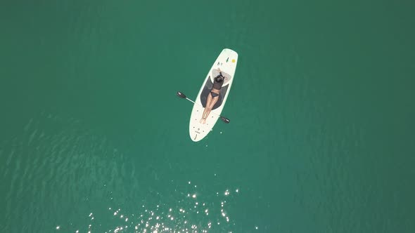 Aerial Shot: Back View of Sexy Brunnette Lying on a Paddleboard at the Blue Sea.