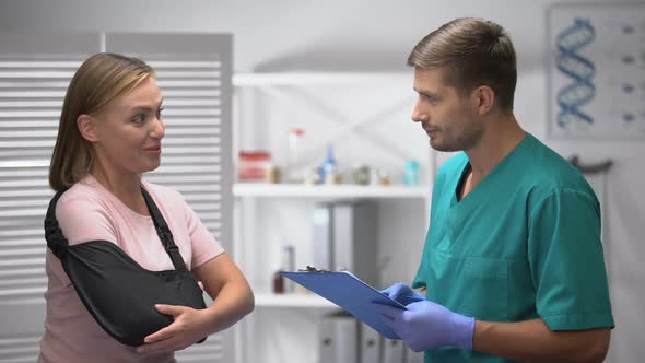 Female in Arm Sling Telling Doctor With Medical Form About Good Rehab Results