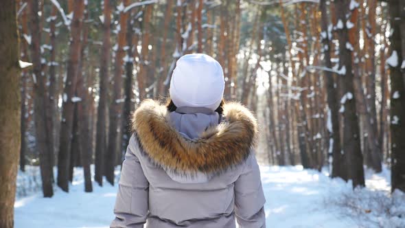 Back View of Woman Walking in Sunny Snowy Forest
