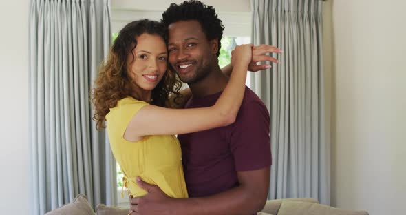 Portrait of happy biracial couple looking at camera, embracing and smiling