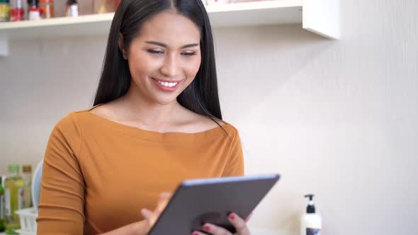 Young woman relaxing standing in kitchen and using digital tablet.