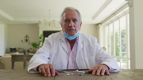 Portrait of caucasian senior male doctor with lowered face mask talking looking at the camera