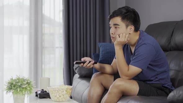 young bored man watching tv and sitting on sofa in the living room