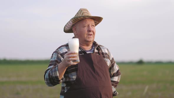 Senior Worker in Apron Holding Drinking Beer at Field