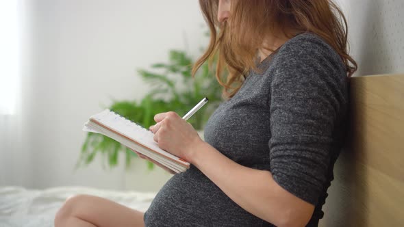 Pregnant Woman Takes Notes in a Notebook Makes a List of Necessary Things for Pregnancy Childbirth
