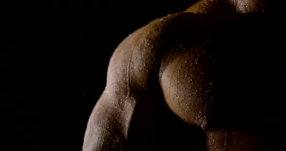 Close Up of Muscular Chest Arm and Shoulder of a Professional Bodybuilder in the Dark in the Rain