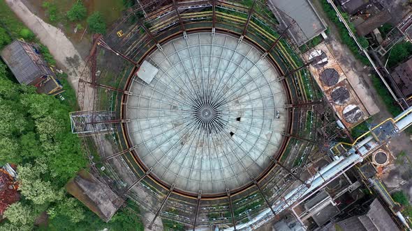 Aerial top-down view of storage tank at abandoned steel factory. Rotating while flying up to reveal