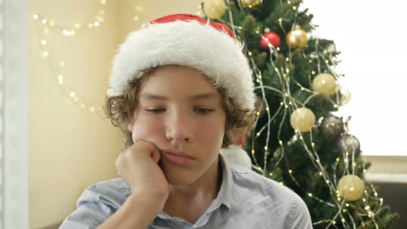 Portrait of a Teenage Boy Wearing a Santa Hat Who Is Bored or Sad. Against the Background of the