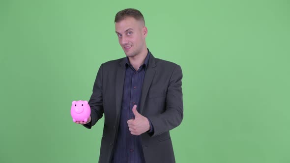 Happy Handsome Businessman in Suit Holding Piggy Bank and Giving Thumbs Up