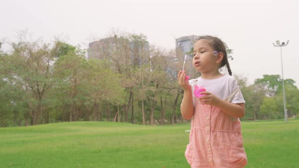 Happy little girl kid blowing soap bubbles playing alone in the park