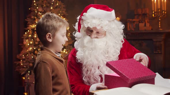 Santa Claus and little boy. Cheerful Santa is working at the table. Christmas concept.