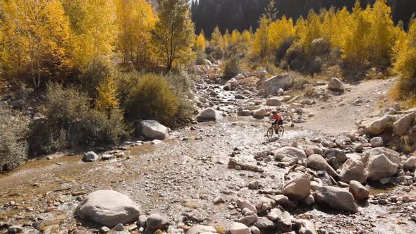 Man Is Crossing the River By Bicycle in the Mountains Shot By Drone