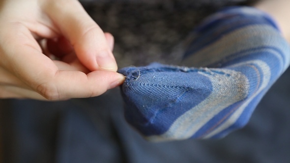 A Woman Sews Up Holes in Socks