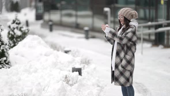 Young Happy Woman Is Strolling in Town at Winter Throwing Snowball at Camera Smiling Happily