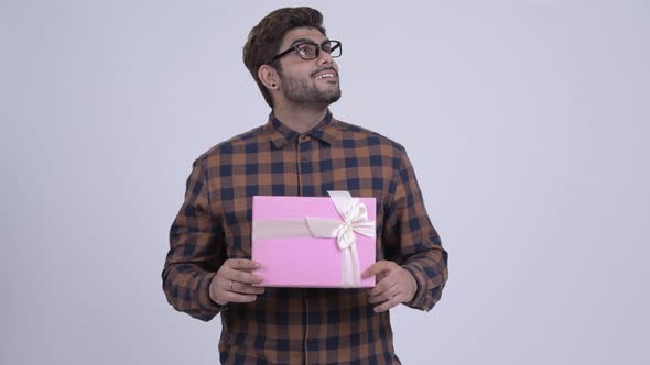 Happy Young Bearded Indian Hipster Man Holding Gift Box and Thinking
