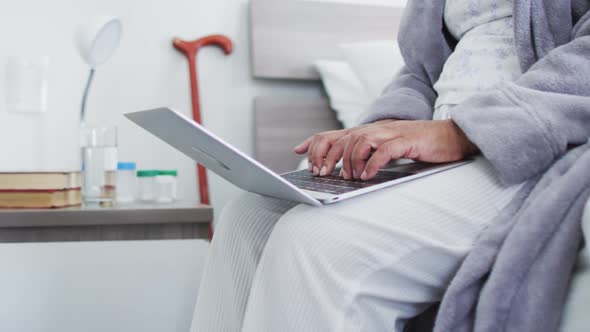 Mid section of african american senior woman using laptop while sitting on the bed at home
