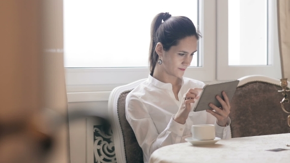 Woman Using Tablet And Drinking Coffee By Table 