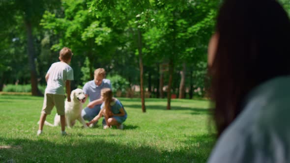 Woman Watching Family Play with Dog in Park Blurred View