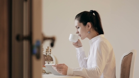 Woman Using Tablet And Drinking Coffee By Table 